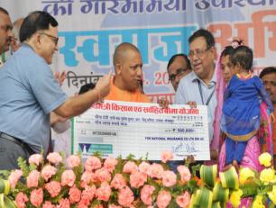 उत्तर प्रदेश के मुख्यमंत्री योगी आदित्यनाथ जी 29 अप्रैल, 2018 को जनपद गोरखपुर में भारतीय स्टेट बैंक द्वारा आयोजित ग्राम स्वराज अभियान के शुभारम्भ कार्यक्रम अवसर पर एक महिला लाभार्थी को मुख्यमंत्री किसान एवं सर्वहित बीमा योजना का चेक प्रदान करते हुए।